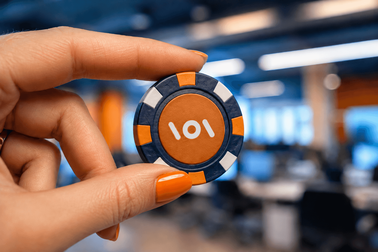Hand holding a blue and orange branded casino chip in a modern iGaming office environment